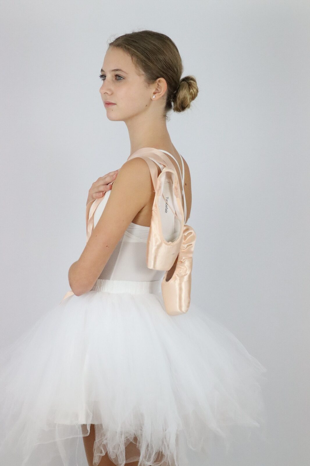 Ballerina mit Ballettschuhen auf den Schultern steht im Fotostudio