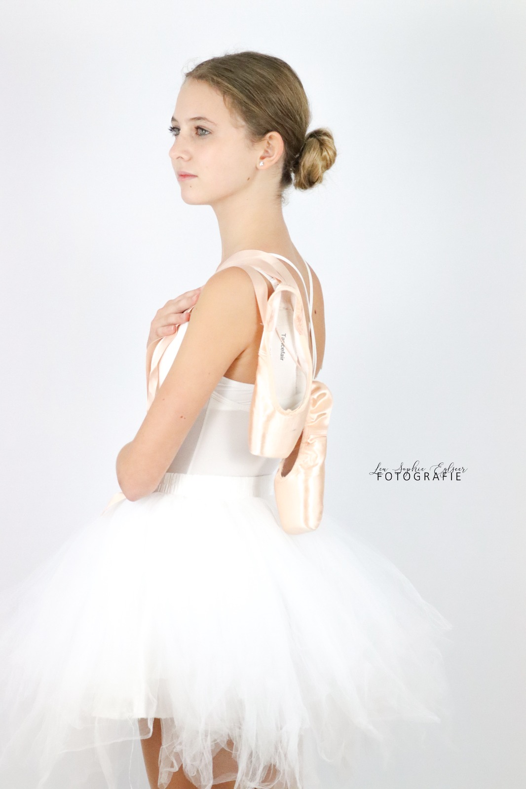 Ballerina mit Ballettschuhen auf den Schultern steht im Fotostudio